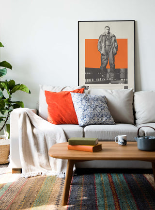 Nas poster on wall above a cozy living room sofa with colorful cushions.